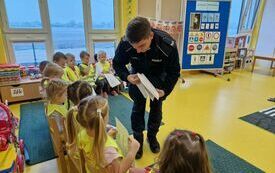 Pan policjant rozdaje dzieciom kolorowanki.
