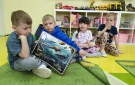 Dzieci oglądają książkę o dinozaurach.